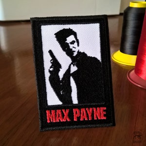 May include: Black and white embroidered patch of Max Payne holding a gun with the text "Max Payne" in red letters.
