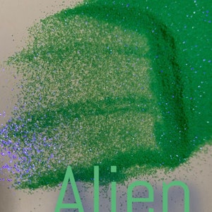 May include: Green glitter with blue iridescent flecks. The word "Alien" is written in green across the image. The glitter is scattered across a white surface, creating a sparkling effect.
