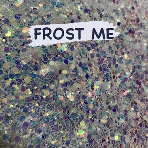 May include: A close-up of iridescent glitter in various shapes and sizes, with a white background and the text "FROST ME" in black.