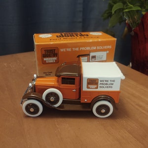 May include: Die-cast metal Ford Model A pickup truck in orange and brown with white wheels. The truck has the text "TRUST WORTHY HARDWARE STORES" and "WE'RE THE PROBLEM SOLVERS" on the side.