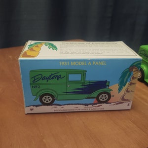 Puede incluir: Un coche de juguete verde y azul 1931 Model A Panel Daytona No. 2 sobre un fondo blanco. La caja tiene una palmera y el texto "Recomendado para mayores de 8 a&ntilde;os."