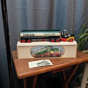 May include: A green and white Hess toy truck with a tanker trailer. The truck has the word "Hess" and "Gasoline" printed on the side. The truck is in its original box, which also features a picture of the truck.