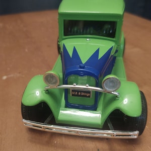 Puede incluir: Coche de juguete verde con un dise&ntilde;o de pintura azul y verde. El coche tiene un parachoques cromado y faros. El coche tiene una matr&iacute;cula que dice "M.B. & Strings".