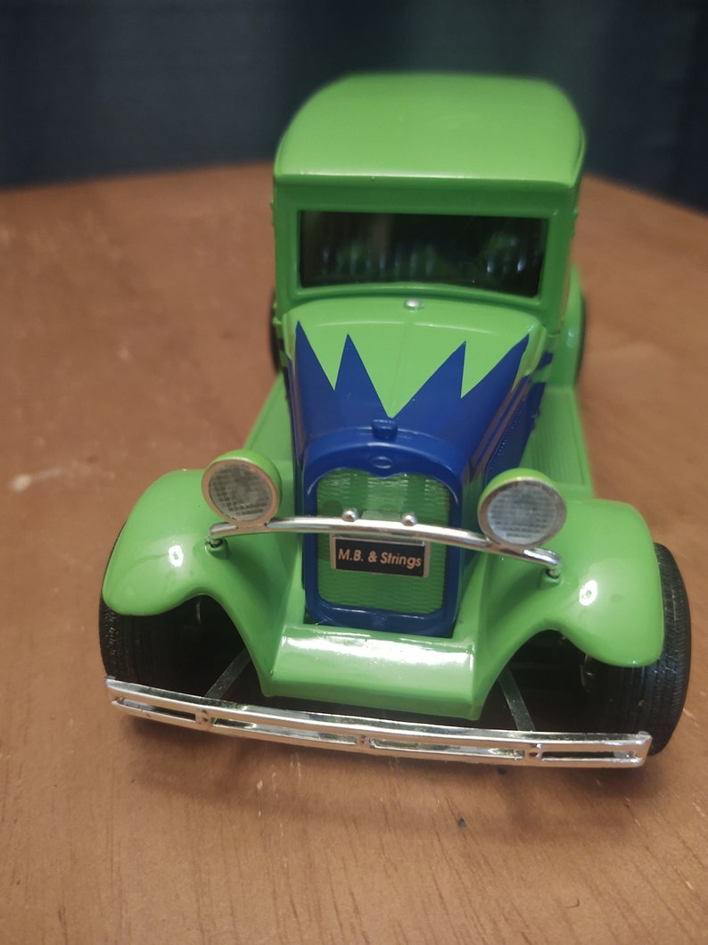 Puede incluir: Coche de juguete verde con un dise&ntilde;o de pintura azul y verde. El coche tiene un parachoques cromado y faros. El coche tiene una matr&iacute;cula que dice "M.B. & Strings".