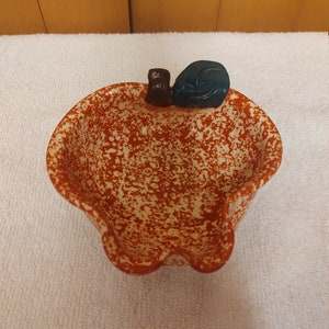 May include: A ceramic bowl shaped like an apple with a speckled brown and white glaze. The bowl has a blue and brown ceramic embellishment on the top.