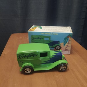 Puede incluir: Un juguete de cami&oacute;n de reparto verde 1931 Model A Panel con una franja azul y "Daytona No. 2" escrito en el lateral. El cami&oacute;n est&aacute; sobre una superficie de madera con una caja detr&aacute;s.