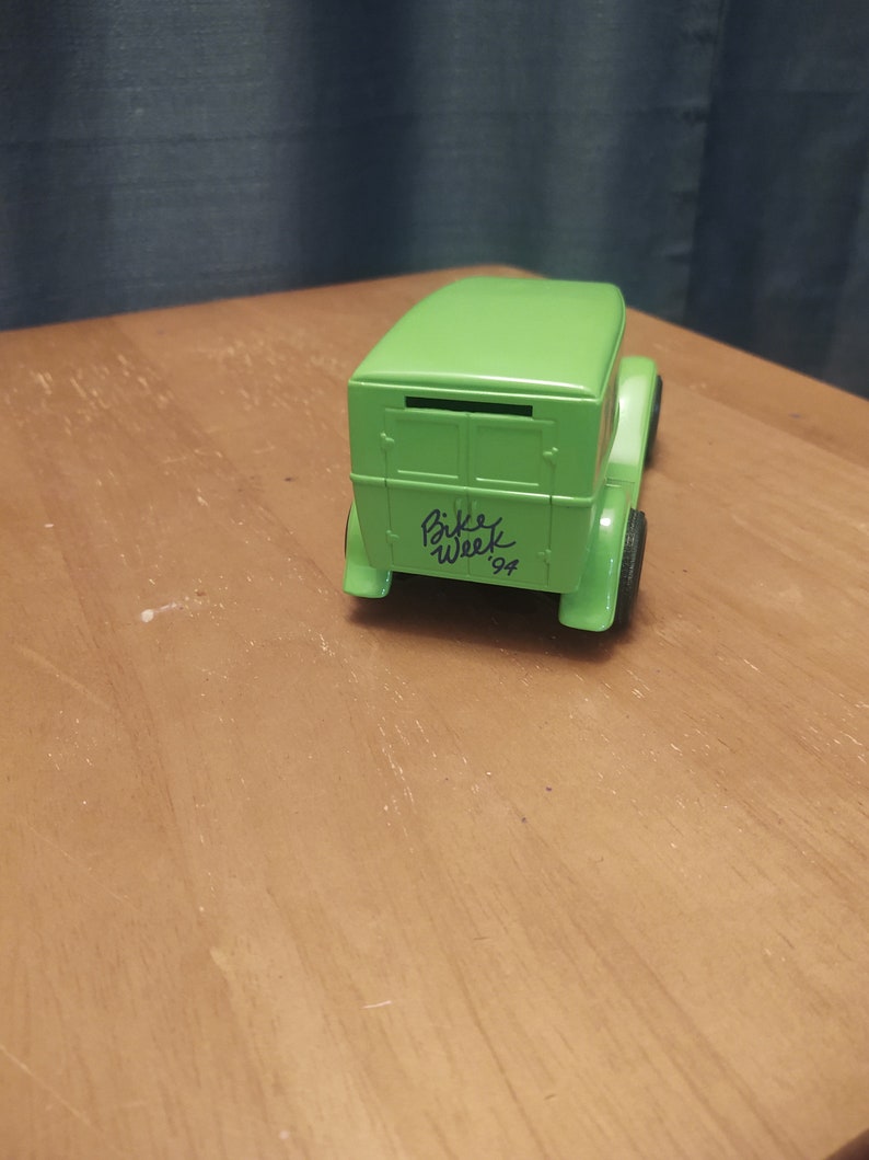 Puede incluir: Modelo de juguete verde de un cami&oacute;n de reparto vintage con una ranura en la parte trasera. El cami&oacute;n tiene escrito "Bike Week '94" en el lateral.