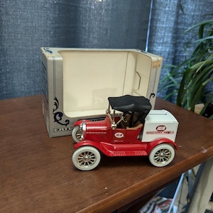 May include: A red toy car with a black canvas top and white wheels. The car has the IGA logo and the text "Hometown Proud" on the side. The car is sitting on a wooden table.