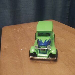 Puede incluir: Un coche de juguete verde con detalles azules y blancos. El coche tiene una parrilla y faros negros. El coche est&aacute; sentado sobre una superficie de madera.