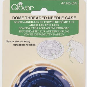 May include: A white plastic dome-shaped needle case with a blue rotating wheel inside. The case is labeled "Clover" and "Art No. 625". The text "Dome Threaded Needle Case" is printed on the front of the case.