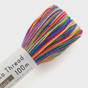 May include: A vibrant skein of embroidery thread in a rainbow of colors. The label reads "Ko Thread 100m MADE IN JAPAN". The thread is tightly wound, showcasing a spectrum of hues including red, orange, yellow, green, blue, and purple, perfect for various craft projects.
