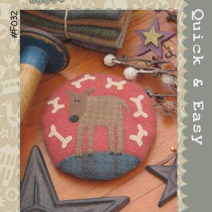 May include: A round, red pincushion with a brown dog and white bone accents. The image also features a stack of fabric, a star, and the text "Digby Dog Pincushion" and "Quick & Easy".
