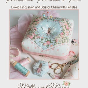 May include: A boxed pincushion and scissor charm set with a felt bee. The pincushion is square, with a floral pattern and a light blue center. Gold scissors and spools of thread are also included. The text reads "Serious Sewist's Set".