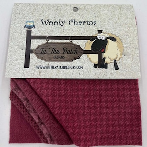 May include: Wooly Charms fabric squares in a deep red color with a subtle herringbone pattern. The fabric is folded in thirds and has a label that reads "In The Patch Designs" and "www.inthepatchdesigns.com".