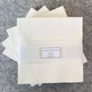 May include: A stack of five cream-colored fabric squares with a label that reads "Essential Solid Cream 5 Kona Gems Washington", a quilting fabric.