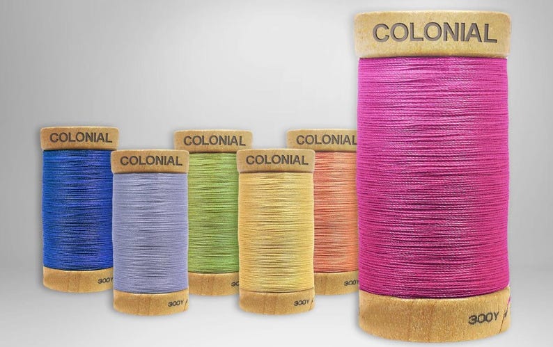 K&ouml;nnte beinhalten: Sechs Garnrollen in verschiedenen Farben, darunter Blau, Lila, Gr&uuml;n, Gelb, Orange und Pink. Jede Rolle ist mit "COLONIAL 300Y" beschriftet.
