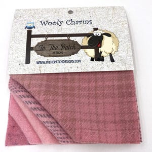 May include: A package of pink and mauve wool fabric squares. The packaging features the text "Wooly Charms" and "In The Patch Designs" with a cartoon sheep and owl. The fabric has a herringbone pattern.