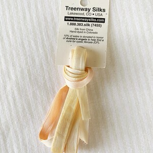 May include: A bundle of silk ribbon in shades of cream and peach, tied with a knot. The ribbon is attached to a white tag with the text "Treenway Silks" and website information. The tag also states the silk is hand-dyed in Colorado.