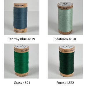 K&ouml;nnte beinhalten: Vier Spulen mit 100% Bio-Baumwollgarn in verschiedenen Blaut&ouml;nen und Gr&uuml;nt&ouml;nen. Die Spulen sind mit "Colonial" und "100% Bio-Baumwolle" beschriftet. Die Farben sind Stormy Blue 4819, Seafoam 4820, Grass 4821 und Forest 4822.