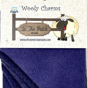 May include: A navy blue fabric with a textured weave is displayed beneath a card featuring the text "Wooly Charms" and "In The Patch Designs." The card includes a cartoon sheep and owl.