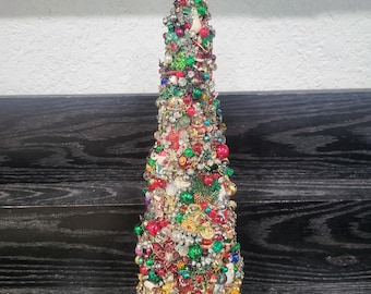 May include: A Christmas tree made of various beads, buttons, and other decorative items. The tree is decorated with red, green, gold, and white ornaments. The tree is about 12 inches tall.