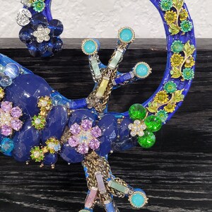 May include: A blue and green mosaic gecko sculpture with colorful flowers and jewels. The gecko is curled up with its tail forming a circle.