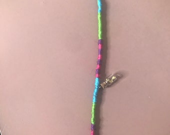 Op de afbeelding: Een kleurrijke haarvlecht met een klein glazen flesje bedel en een boekbedel met de tekst "Alice's Adventures in Wonderland".
