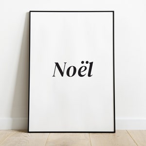 May include: A black framed poster with the word "Noël" in black text on a white background.