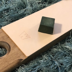 May include: A green sharpening stone on a light pink leather strop with a wooden handle. The strop has the letters "WW" embossed on it.