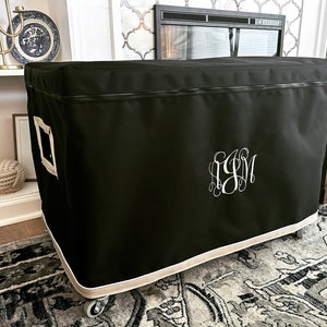 May include: Black storage bin with a beige trim and a zipper closure. The bin has a white monogram "SJM" embroidered on the front. The bin is on wheels and is sitting on a patterned rug.