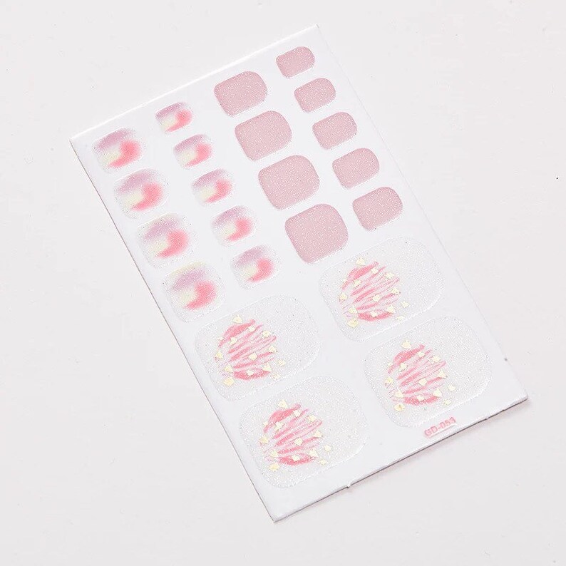 Pu&ograve; includere: Un foglio di adesivi per unghie dei piedi rosa e bianchi con un design glitterato. Il foglio include 12 adesivi individuali per unghie dei piedi e 10 adesivi per unghie dei piedi vuoti.