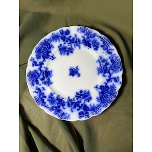 May include: A white and blue floral patterned plate with a scalloped edge. The plate features a central floral design and a border of blue flowers. The plate is round and appears to be made of ceramic.