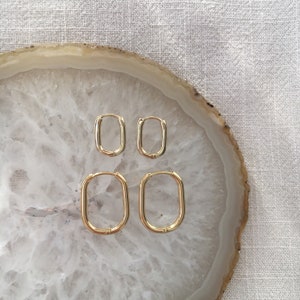 May include: Four gold hoop earrings of different sizes. The earrings are arranged in two pairs, with the smaller pair on top and the larger pair on the bottom. The earrings are on a white agate surface.