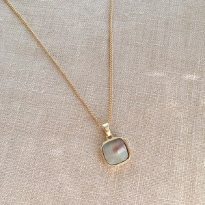 May include: A gold chain necklace with a square-shaped pendant featuring a mother-of-pearl inlay.