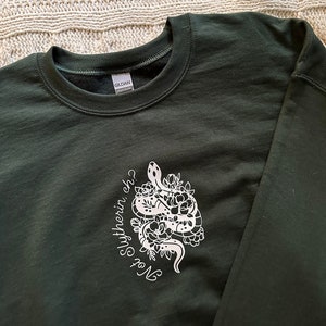 May include: A dark green sweatshirt with a white graphic of a snake with flowers and the text "Not Slytherin, eh?"