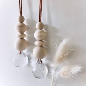 May include: Two wooden bead necklaces with crystal prisms hanging from the bottom. The beads are natural wood and the cords are brown leather.