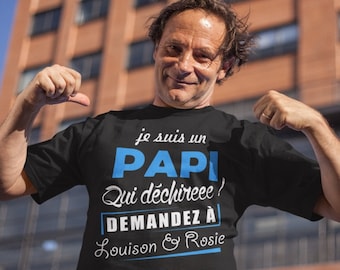May include: Black t-shirt with the text "Je suis un PAPI Qui déchireee ! Demandez à Louison & Rosie" in white and blue. The t-shirt is worn by a person with a building in the background.