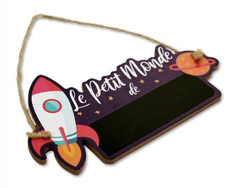 May include: A purple and black wooden sign with a rocket ship and a planet. The sign says "Le Petit Monde de" and has a blank chalkboard space.