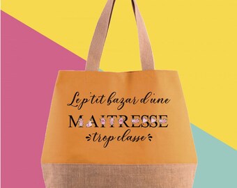 May include: A mustard-colored tote bag with a burlap bottom and tan handles. The bag features the text "Le p'tit bazar d'une MAITRESSE trop classe" in black script with floral accents. The background is a mix of pink, yellow, and teal.