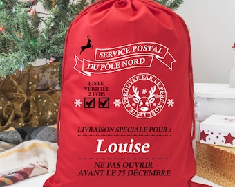 May include: A red Christmas gift bag with white text and a drawstring closure. The bag features text in French, including "Service Postal du Pôle Nord" and the name "Louise". The bag is decorated with snowflakes and a reindeer.