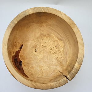 Könnte beinhalten: Eine handgefertigte Holzschale mit natürlicher, hellbrauner Oberfläche. Die Schale weist einzigartige Holzmaserungsmuster und einen dunkelbraunen Knoten auf. Die Schale hat einen Durchmesser von ca. 25 cm und eignet sich ideal zum Servieren oder Ausstellen.