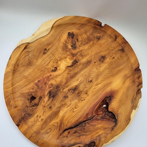 May include: A round, wooden serving tray with a natural edge. The tray is made from a single piece of wood, showcasing the grain and knots. The color is a warm, reddish-brown with lighter, cream-colored edges. The tray has a diameter of approximately 18 inches.