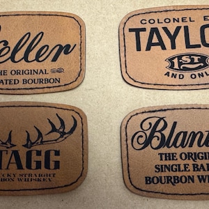 May include: Four brown leather patches with black text. The patches feature the names "Weller", "Taylor", "Stagg", and "Blanton's", along with additional text indicating the type of bourbon. The patches have a stitched border.