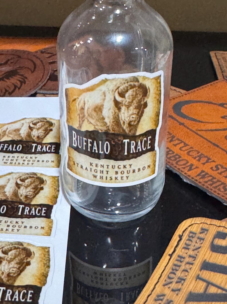 May include: A clear glass bottle with a label that says "Buffalo Trace Kentucky Straight Bourbon Whiskey". The label features a brown and white illustration of a buffalo.
