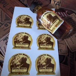 May include: A small bottle of amber-colored liquor with a black cap, labeled "Pappy Van Winkle's Family Reserve 15 years old." Several matching oval stickers are visible. The background includes leather tags.