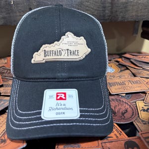 May include: Black and white trucker hat with a patch that reads "Buffalo Trace" and a Kentucky outline. The hat has a white mesh back and a curved brim. A tag on the front reads "It's a Richardson OSFM".