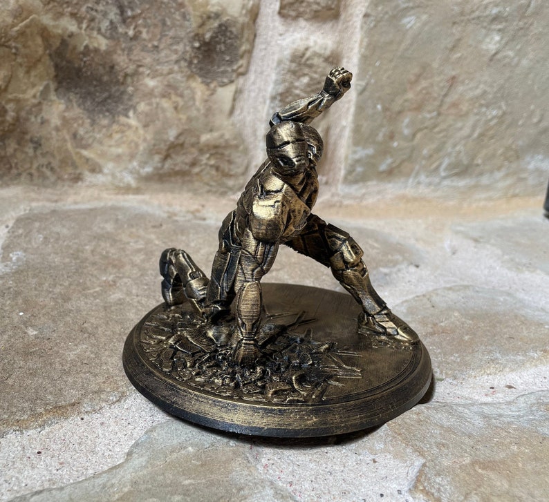 May include: A gold-painted figurine of a person in a dynamic pose, standing on a circular base with a textured surface.