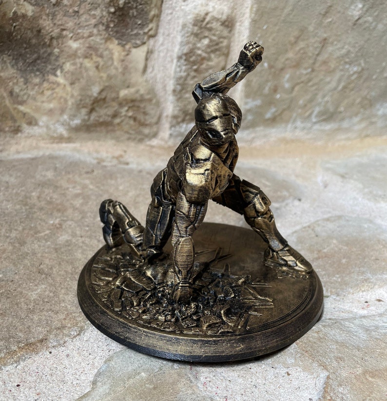 May include: A gold-painted figurine of a robot in a dynamic pose, standing on a circular base with a textured surface. The robot has a detailed design and appears to be made of plastic.