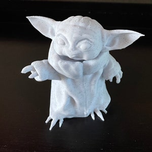 May include: A 3D-printed figurine of a character with large ears and a robe. The figure is white with small black speckles, and has its arms outstretched. The figurine is a popular character from a science fiction franchise.