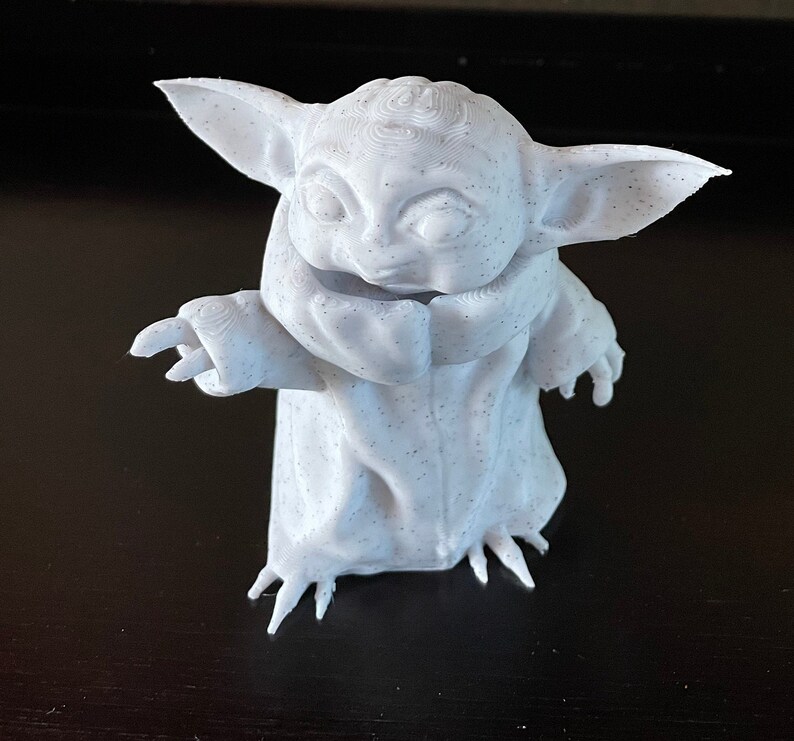 May include: A 3D-printed figurine of a character with large ears and a robe. The figure is white with small black speckles, and has its arms outstretched. The figurine is a popular character from a science fiction franchise.